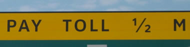 Upper left is a rectangular warning panel that displays the legend "PAY TOLL" in the alternative alphabet in a negative-contrast orientation.