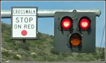 Shows a three-section pedestrian hybrid beacon face mounted near the end of a mast arm with both of the two horizontally-arranged circular red indications illuminated.