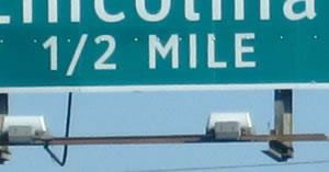 The image is of part of road sign with a green background and white lettering.  The legible part reads: 1/2 MILE. The 1 and 2 are side by side.