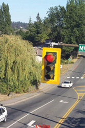 photo depicting signal head with reflective backboard,highly visible against daytime background.